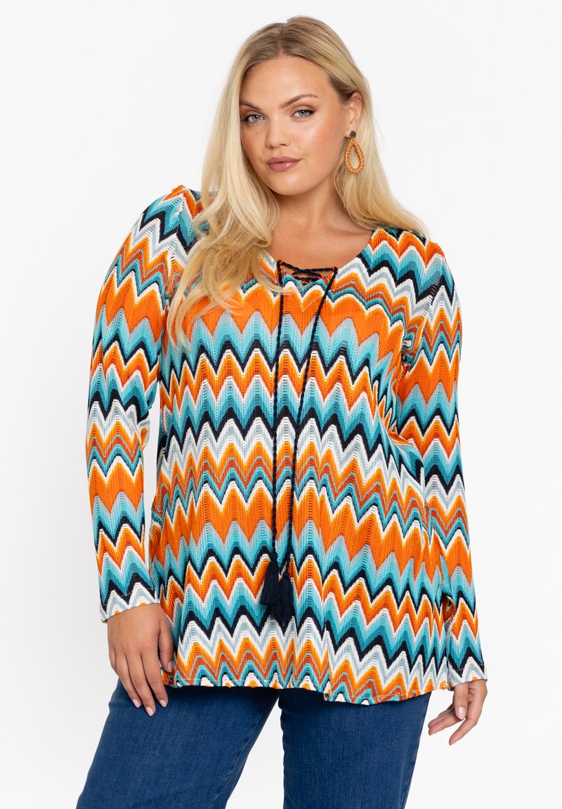 Meerkleurige blouse met lange mouwen, voorzien van een zigzagpatroon in oranje, teal, zwart en wit, met een ronde halslijn en een trekkoorddetail.
