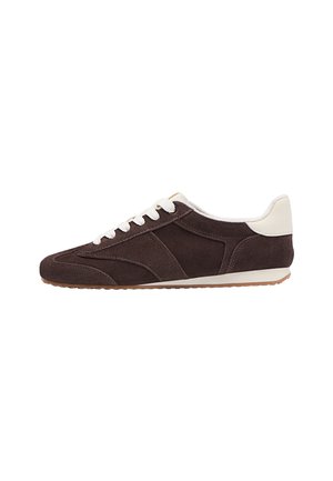 Sneaker in suede marrone con lacci e inserti sul tallone bianchi, suola in gomma a profilo basso, esposta in vista laterale su sfondo bianco.