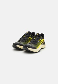 Baskets de trail noires et jaunes avec un dessus en maille texturée, une semelle rembourrée et des motifs robustes pour l'adhérence et la stabilité.