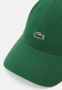 Grønn baseballcap laget av teksturert stoff, med et sydd logoaktsent og synlige sømdetaljer på skyggen.