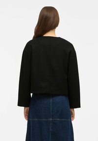 Maglione nero cropped con maniche ampie, realizzato in tessuto testurizzato. Presenta un collo semplice e cuciture pulite, abbinato a una gonna di denim.