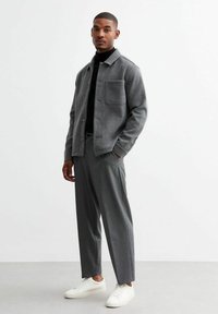 Giacca grigia e strutturata con tasca sul petto, abbinata a pantaloni a quadri grigi e sneakers bianche. Design slim-fit e hardware minimale.