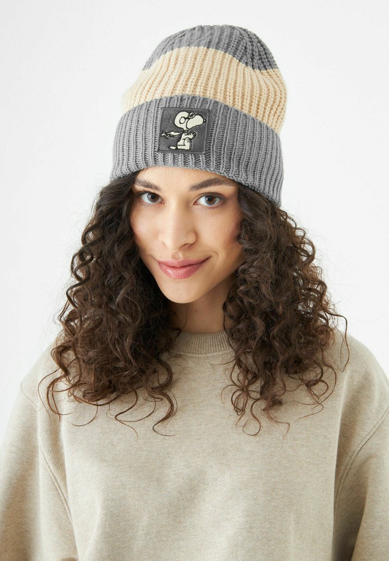Grijze en beige gestreepte gebreide muts met een patch van een cartoonfiguur. De stof is geribbeld en zacht, met een snug fit.