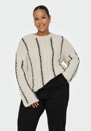 Dicker, creamfarbener gestrickter Pullover mit schwarzen vertikalen Streifen und gerippten Akzenten; verfügt über einen runden Halsausschnitt und weite Ärmel, kombiniert mit schwarzen Hosen.