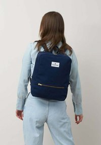 Zaino in tela navy con design piatto, dettagli della cerniera dorati e una tasca frontale. Topo logo al centro della parte superiore del bag.
