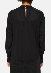Sort langærmet bluse med smocket hals, der har en nøglehulslukning bagpå og en pyntet forsom for en afslappet pasform. Blødt stof.