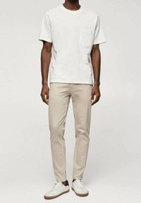 Camiseta de algodón blanca con un bolsillo en el pecho, combinada con pantalones slim-fit beige claros y zapatillas blancas con detalles en marrón.