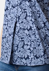 Blusa floreale in azzurro chiaro con motivo floreale blu navy; presenta una vestibilità ampia e spacchi laterali; realizzata in tessuto leggero.