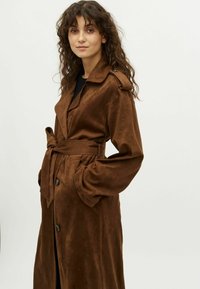 Bruine, ceintuurtrenchcoat van zacht materiaal. Heeft een gekarteld kraag, zijzakken en een knoopsluiting. Lange mouwen met manchet.