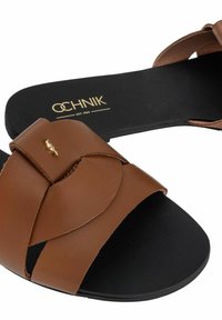 Brązowe skórzane sandały na płaskiej podeszwie z krzyżującymi się paskami, z ozdobą w kolorze złotym i czarną gumową podeszwą.