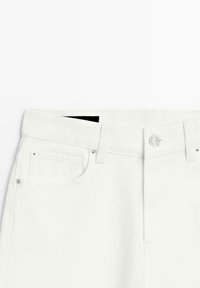 Vita e parte superiore di jeans in denim bianco con tasche anteriori, passanti per cintura e chiusura con bottone metallico.