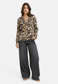 Bluse mit Leopardenmuster in Brauntönen und Beige, kombiniert mit weit geschnittenen, dunklen Jeans. Weicher Stoff, lockere Passform und V-Ausschnitt.