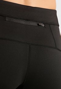 Leggings deportivos negros con una textura suave, cintura alta y un pequeño bolsillo con cremallera en la parte posterior para un almacenamiento seguro.