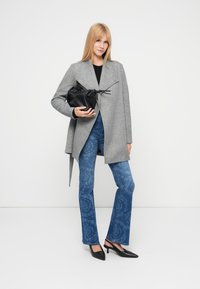 Παλτό γκρι από μείγμα μάλλινου υφάσματος με ασύμμετρο τελείωμα, συνδυασμένο με μπλε τζιν με λουλουδάτο μοτίβο και μαύρο πουγκί με κορδόνι. Μαύρες μυτερές γόβες.