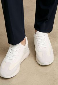 Sneaker bianche con un mix di pannelli lisci e testurizzati, dotate di una suola spessa, punta rotonda e design con lacci. Design minimalista e moderno.
