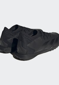 Zapatillas deportivas negras con parte superior de textil, detalles texturizados y una suela de goma firme con tacos de tracción. Cintas aseguradas en la parte superior.