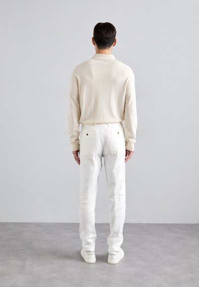 Beige striktrøje med lange ærmer, hvide slim-fit bukser med baglommer og hvide sko; minimalistisk design med neutrale farver.