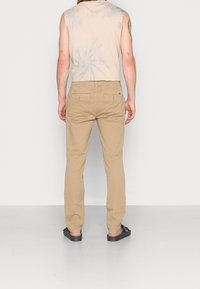 Beige bomullsbukser med rak passform, med två bakfickor och uppvikt fåll, tillsammans med en ärmlös top med tie-dye-mönster.