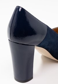 Scarpa con tacco alto navy in pelle verniciata lucida, con tomaia in suede testurizzato, punta arrotondata e soletta beige.