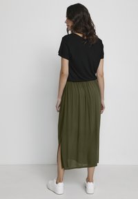 Black short-sleeve top paired with a green, pleated maxi skirt featuring a side slit, worn with white sneakers. Simple and loose-fitting design.