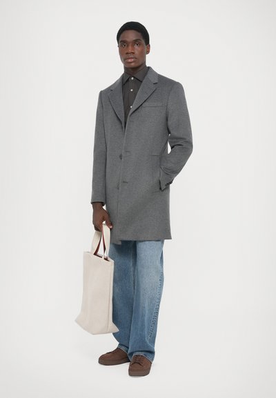 Grå ullkappa med klädd krage, enknappstängning och sidofickor, bärs över en mörk skjorta och kombineras med vida blå jeans.