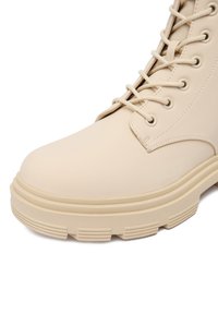 Beżowe sznurowane botki, wykonane z gładkiego materiału syntetycznego, z okrągłym noskiem, żebrowaną podeszwą i kontrastującymi przeszyciami.
