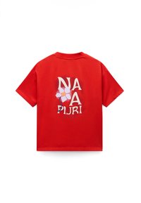 Κόκκινο βαμβακερό μπλουζάκι με γραφικό σχέδιο στην πλάτη που περιλαμβάνει το κείμενο "NA NA PLIURI" και μια εικονογράφηση λουλουδιού με ροζ και μπλε αποχρώσεις.
