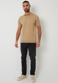 Béžová polo košile s krátkým límečkem, přiléhavým střihem a hladkou texturou. Kombinována s tmavými džíny a světlými teniskami.