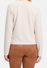 Long-sleeve cream top with a ribbed texture, featuring a round neckline and a straight hem, paired with brown suede-like pants.
