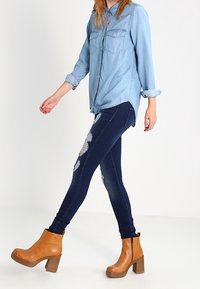 Ljusblå denimskjorta med långa ärmar och två bröstfickor, som kombineras med mörkblå slitna skinny jeans och tanfärgade klackade ankelboots.