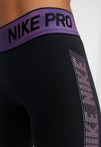 Czarne legginsy sportowe z fioletowym gradientowym pasem w talii, na którym znajduje się napis "NIKE PRO". Ciekawym akcentem jest kropkowany wzór po boku.