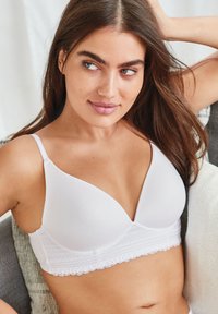 Bralette blanche en tissu lisse et doux, dotée d'une accent en dentelle le long du bas. Elle a des bretelles réglables et une forme de coque triangulaire.