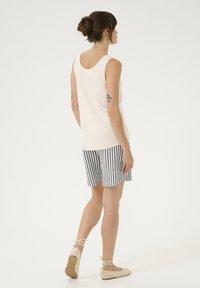 Ljus beige linne med rund halsringning, kombinerat med svart-vita randiga shorts och vävda snörade espadriller. Slät textur och avslappnad passform.