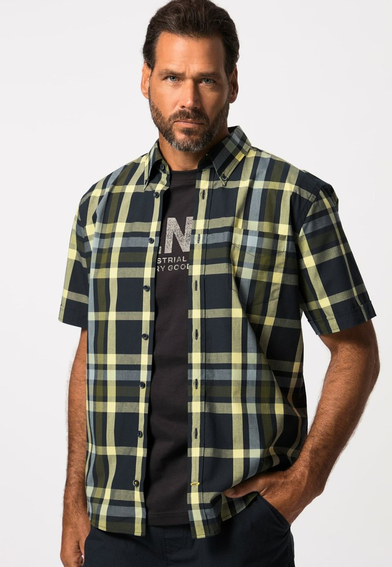 Kurzärmliges Karhemd in Gelb-, Marineblau- und Grüntönen; mit einem Button-Down-Kragen und einer Brusttasche; kombiniert mit einem dunklen T-Shirt darunter.