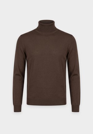 Femme portant un pull à col roulé marron, un pantalon bleu droit, des chaussures plates marron, un collier de perles et un sac à bandoulière marron texturé.