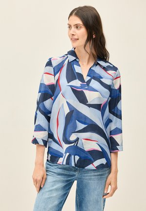 Blouse à motifs bleus et blancs avec un col, manches trois-quarts, présentant des formes abstraites et des accents rouges, tissu texturé, coupe décontractée.
