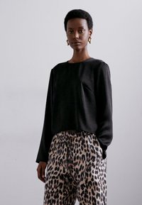 Cămașă neagră cu mâneci lungi și croială scurtă, cu un finisaj texturat, asociată cu pantaloni bej cu imprimeu leopard, având talie elastică.