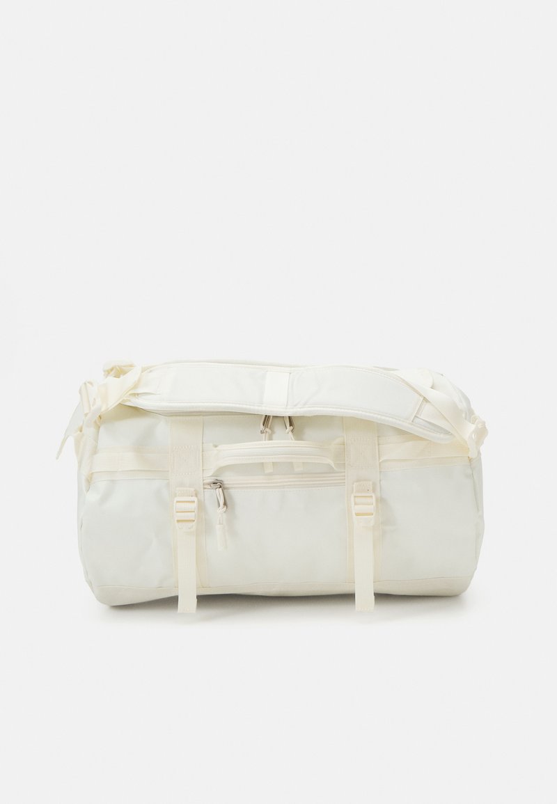 Sac de sport en tissu léger couleur écru, avec plusieurs sangles, une poche zippée à l'avant et une forme cylindrique.