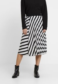 Jupe midi à rayures noires et blanches avec une taille élastique ; texture lisse ; associée à des bottines noires avec un motif crocodile.