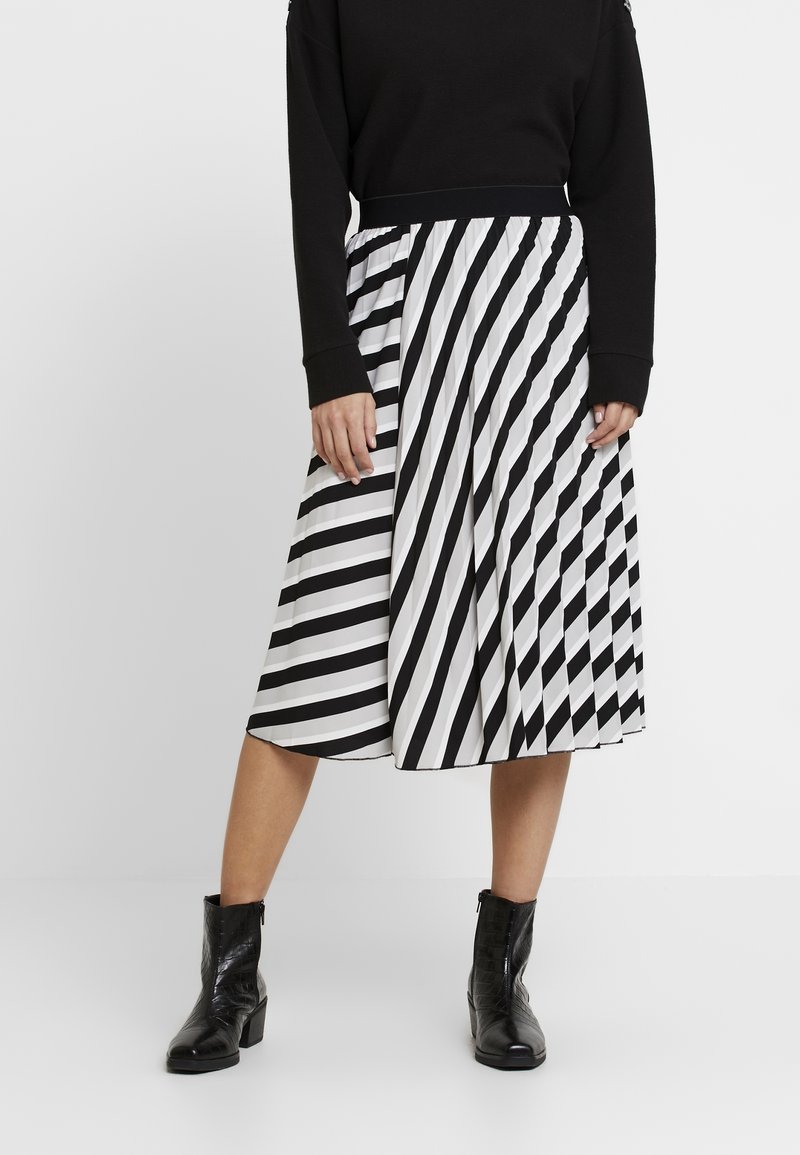 Jupe midi à rayures noires et blanches avec une taille élastique ; texture lisse ; associée à des bottines noires avec un motif crocodile.