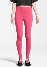 Leggings rosa realizzati in tessuto elastico, con un alto punto vita e un logo discreto sul lato, abbinati a scarpe da ginnastica nere.