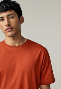 Kortærmet t-shirt med rund hals i ensfarvet brændt orange bomuld, der har en glat overflade og diskrete syninger langs udskæringen.