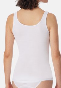 White tank top featuring a fitted design, soft cotton material, thin straps, and a rounded neckline, showcased from the back.
