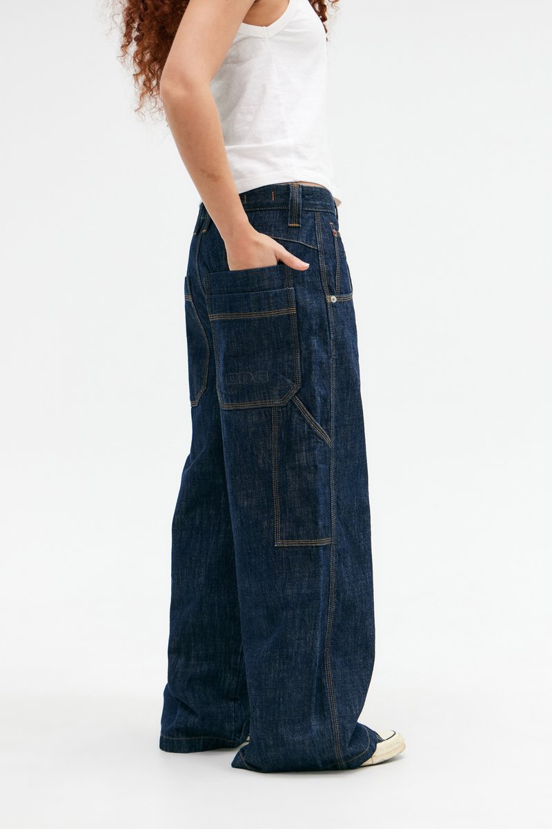 Jeans denim a gamba larga in blu scuro, con ampie tasche, cuciture a contrasto e una vestibilità rilassata. Il tessuto presenta un aspetto leggermente strutturato.
