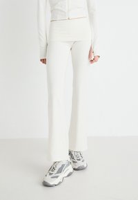 Leggings bianchi aderenti con fondo svasato, design senza cuciture, abbinati a sneaker grigie e bianche con suola spessa, su uno sfondo bianco uniforme.