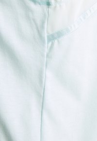 Jasnoniebieska tkanina o gładkiej teksturze, z siateczkową wstawką i kontrastowym przeszyciem. Projekt zawiera szczegół z zaokrąglonym szwem.