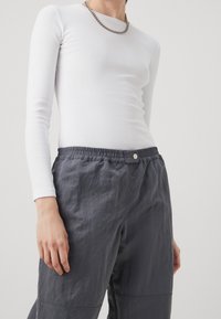 Top bianco a maniche lunghe abbinato a pantaloni leggeri elastici grigio scuro con vita elastica, dotati di bottone a pressione e tessuto texturizzato.