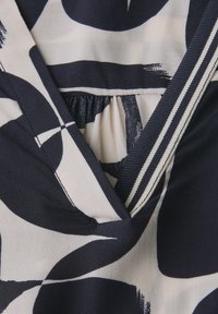 Gros plan d'un tissu à motif abstrait noir et blanc avec des coutures surpiquées et une section froncée près d'un décolleté en forme de V.