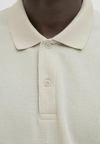 Polo de color verde claro con un diseño texturizado de punto waffle, que presenta un collar suave y dos botones de un color claro a juego.