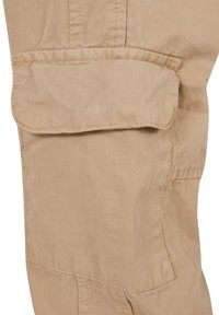 Beige Cargo-Hosenabschnitt mit einer Klappentasche, sichtbaren Nahtdetails und einer strukturierten Stoffoberfläche.